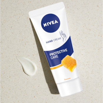 NIVEA Protective Care krem do rąk, biała tubka z niebieskim i miodowym wzorem, leży ukośnie na jasnym blacie, obok kropla kremu.