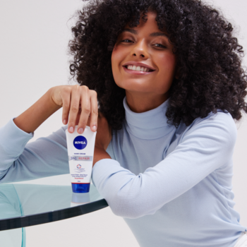 Regeneracyjny krem NIVEA Repair Care 75ml w biało-niebieskiej tubce, trzymany przez uśmiechniętą kobietę.