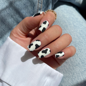 Dłoń z paznokciami w czarno-białe łaty, matowe wykończenie. Do wzoru użyto lakier Semilac 001 Strong White.