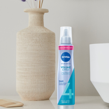 NIVEA Volume & Hold Pianka do włosów, fioletowo-turkusowa butelka z białym dozownikiem, obok beżowej wazy.