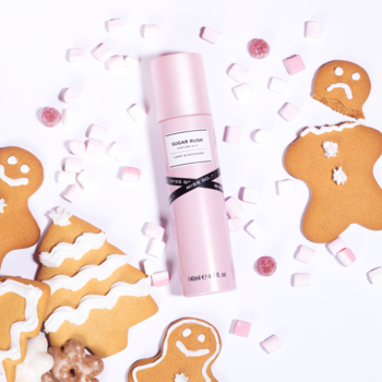 Mgiełka perfumowana Miss So...? Sugar Rush, różowa butelka z czarną kokardką, otoczona świątecznymi piernikami i słodyczami na białym tle.