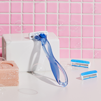 Niebieska damska maszynka BIC Click Soleil 3 z 3 ostrzami i zakrzywioną rączką, na blacie obok wkładów, różowe płytki.