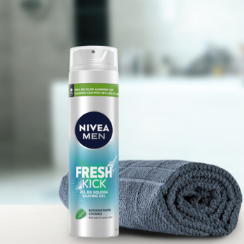 NIVEA MEN Fresh Kick żel do golenia, biało-niebieska butelka, zielone akcenty, obok szary ręcznik, widok z przodu na blacie w łazience.