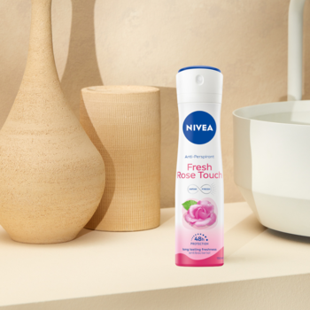 Biały antyperspirant NIVEA Fresh Rose Touch w sprayu, z różą, na beżowym tle z wazonami, widok z przodu.