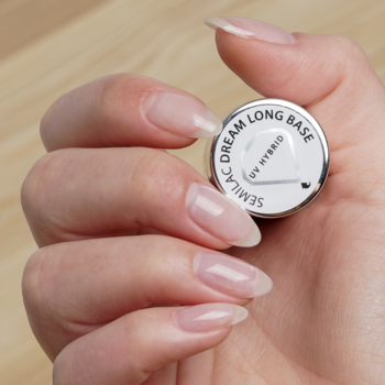 Zbliżenie na dłoń z długimi, naturalnymi paznokciami trzymającą okrągłą bazę Semilac Dream Long Base UV Hybrid.