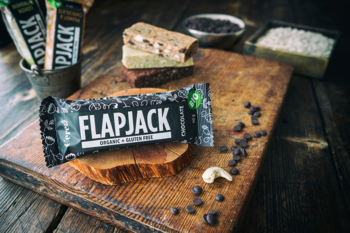 Ekologiczny pieczony baton owsiany Flapjack, z nerkowcami i czekoladą na drewnianej desce z rozsypanymi składnikami.