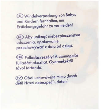 Zbliżenie na czarne opakowanie pieluszek premium, ostrzeżenia o ryzyku uduszenia w językach PL, DE, HU, CZ.