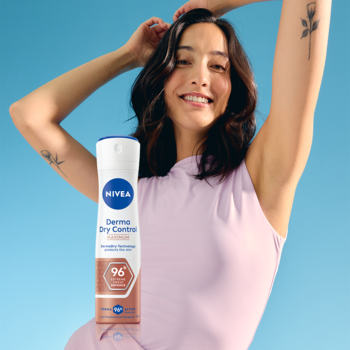 Uśmiechnięta kobieta w liliowym topie trzyma biało-brązowy spray NIVEA Derma Dry Control 96h na niebieskim tle.