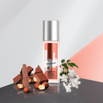 Różowy dezodorant Bruno Banani Magnetic Woman w sprayu, obok czekolada z orzechami i jaśmin, na dwukolorowym tle.