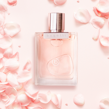 Perfumy Bugatti Bella Donna w szklanej butelce z różowym płynem, napisem "bugatti" na metalowej nakrętce, na tle różowych płatków.