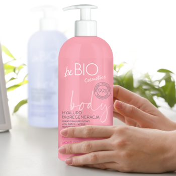 Różowa butelka balsamu beBIO Hyaluro bioRegeneracja 99% naturalny, z pompką, trzymana w dłoniach.