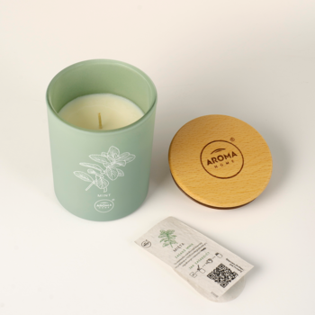 Aroma Home świeca miętowa w zielonej szklance, obok drewniana pokrywka i zasiewana zawieszka „plant me”.