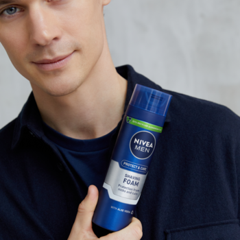 Mężczyzna trzyma niebiesko-srebrną piankę do golenia NIVEA MEN Protect & Care w puszce, widok z przodu.