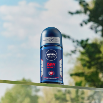 NIVEA MEN Dry Impact antyperspirant w kulce 72h, niebieska butelka na rozmytym tle zieleni i błękitnego nieba.