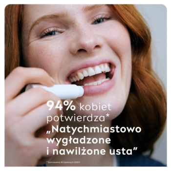 Uśmiechnięta kobieta aplikuje białą nawilżającą pomadkę NIVEA Original Care w sztyfcie do ust. Bliskie ujęcie.