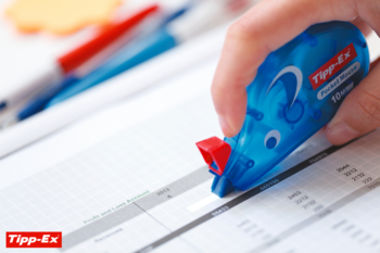 Ręka używa niebieskiego korektora w taśmie Tipp-Ex Mouse 4,2mm na dokumencie, blisko napisu Profit.