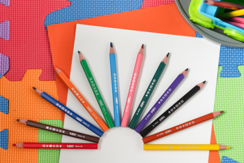 10 trójkątnych kredek XL dla dzieci ułożonych wachlarzowo na białym papierze, na kolorowym tle piankowym.