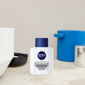 NIVEA MEN Silver Protect Balsam po goleniu w białej butelce z niebieską nakrętką, widok z przodu na tle łazienki.