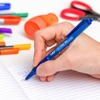 Ręka pisze niebieskim długopisem automatycznym BIC Soft Feel 0.8mm z gumowym uchwytem w zeszycie.