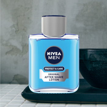 NIVEA MEN Protect & Care Original After Shave Lotion w niebieskiej kwadratowej butelce na tacy, widok z przodu.