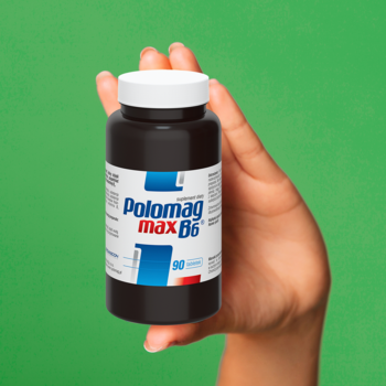 Ciemna butelka suplementu Polomag max B6 z niebiesko-białą etykietą, trzymana w dłoni, na zielonym tle, widok z przodu.