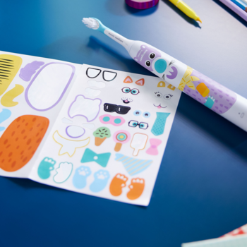 Biała szczoteczka soniczna Philips Sonicare For Kids z kolorowym wzorem, obok arkusz naklejek na granatowym blacie.