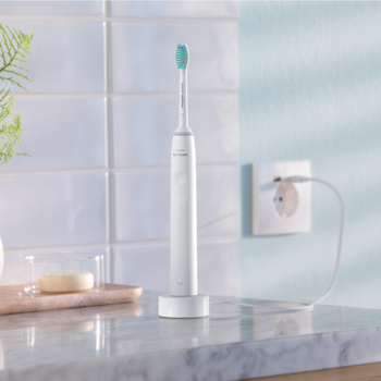 Biała szczoteczka soniczna Philips Sonicare z turkusową główką na ładowarce, na marmurowym blacie.