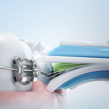 Zbliżenie główki szczoteczki Philips Sonicare W2 Optimal White, czyści ząb z aparatem. Biało-niebieskie włosie.