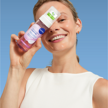 Uśmiechnięta kobieta trzyma różową piankę oczyszczającą NIVEA do twarzy, dedykowaną do wrażliwej skóry.