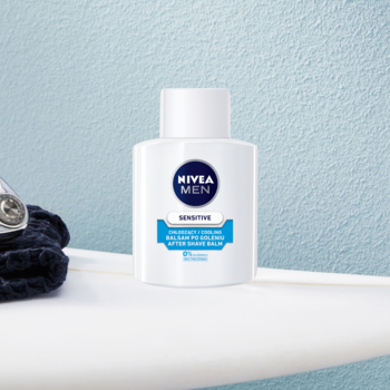 NIVEA MEN Sensitive Chłodzący Balsam po goleniu, biała butelka na półce, obok ciemny ręcznik.