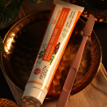 Ayurvedic Total Care ziołowa pasta w białej tubce z pomarańczem, z różową szczoteczką na złotej tacy.