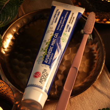Naturalna miętowa pasta AYURVEDIC MINT GEL w białej tubce z różową szczoteczką, leżące na złotej tacy.