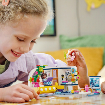 Uśmiechnięta dziewczynka bawi się kolorowym zestawem klocków LEGO Friends, budując mały domek z meblami.