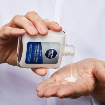 Męskie dłonie z butelką balsamu po goleniu NIVEA MEN Anti-Age Hyaluron, wyciskającego biały krem.