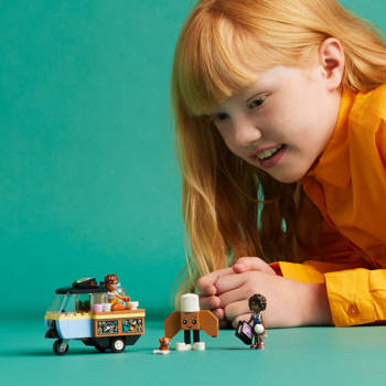 Uśmiechnięta dziewczynka bawi się zestawem Lego Friends Mobilna piekarnia: food truck, minilaleczki, piesek.