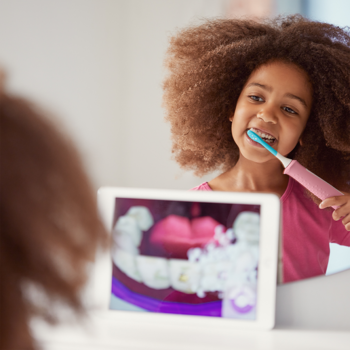 Dziecko myje zęby różową szczoteczką Sonicare For Kids, śledząc postęp w interaktywnej aplikacji na tablecie.
