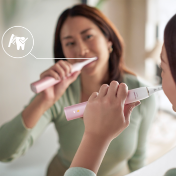 Kobieta szczotkuje zęby różową Sonicare DiamondClean 9000, dla bielszych zębów, widoczne odbicie w lustrze.