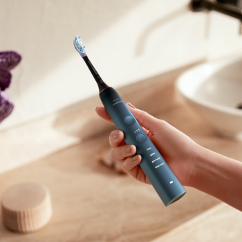 Ciemnoniebieska szczoteczka soniczna Philips Sonicare DiamondClean 9000 trzymana w dłoni w łazience.