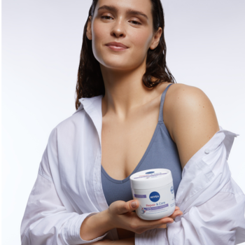 Kobieta z uśmiechem trzyma biało-fioletowy słoik NIVEA Repair&Care Sensitive nawilżająco-ochronnego kremu.