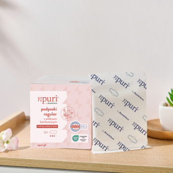 Podpaski higieniczne Npuri regular z bambusem, różowo-białe pudełko i rozpakowana sztuka na drewnianej tacy.