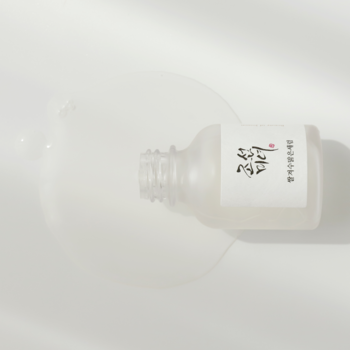 Leżąca butelka Beauty of Joseon Glow Deep Serum z wylanym płynem na przebarwienia, na białym tle.
