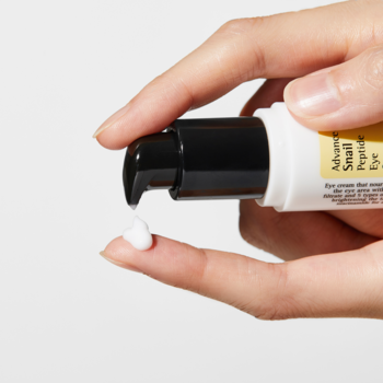 COSRX Advanced Snail Peptide Eye Cream, zbliżenie na dłoń wyciskającą biały krem z żółtej butelki z pompką.
