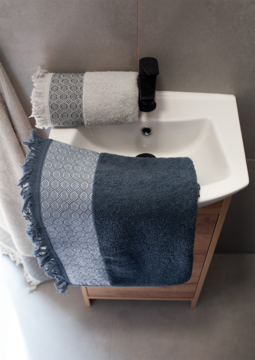 Widok z góry: miękki popielaty ręcznik bawełniany 50x90 z frędzlami, częściowo złożony, na brzegu białej umywalki.