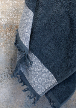 Miękki bawełniany ręcznik w kolorze ciemny popiel, z ozdobnym jasnym pasem i frędzlami, zbliżenie.