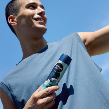 Uśmiechnięty mężczyzna trzyma NIVEA MEN Cool Marine antyperspirant w aerozolu, błękitne tło, widok z bliska.