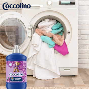 Coccolino Perfume & Care płyn Purple Orchid & Blueberries, niebieska butelka obok pralki z praniem.