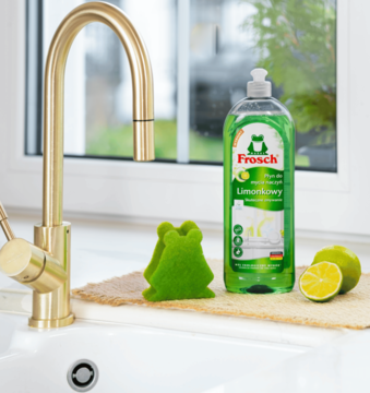 Zielony płyn Frosch Limonkowy do naczyń, wegański, na blacie obok złotego kranu, z limonką i gąbką-żabą.