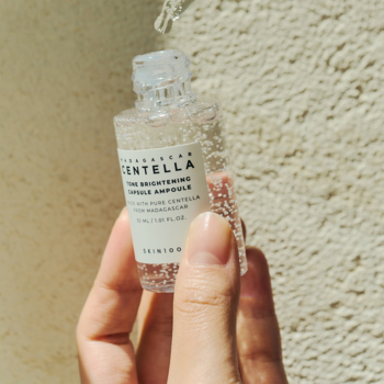 SKIN1004 Centella 77% rozjaśniające serum na przebarwienia, kropla z pipety, trzymane na beżowej ścianie.