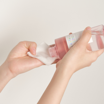 Dłonie wylewają różowy tonik normalizujący Skin 1004 Madagascar Centella z butelki na biały wacik.
