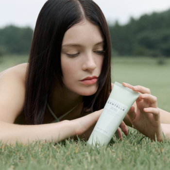 Kobieta na trawie z zieloną tubą pianki SKIN1004 Madagascar Centella Tea-Trica, delikatnie oczyszczającej skórę.